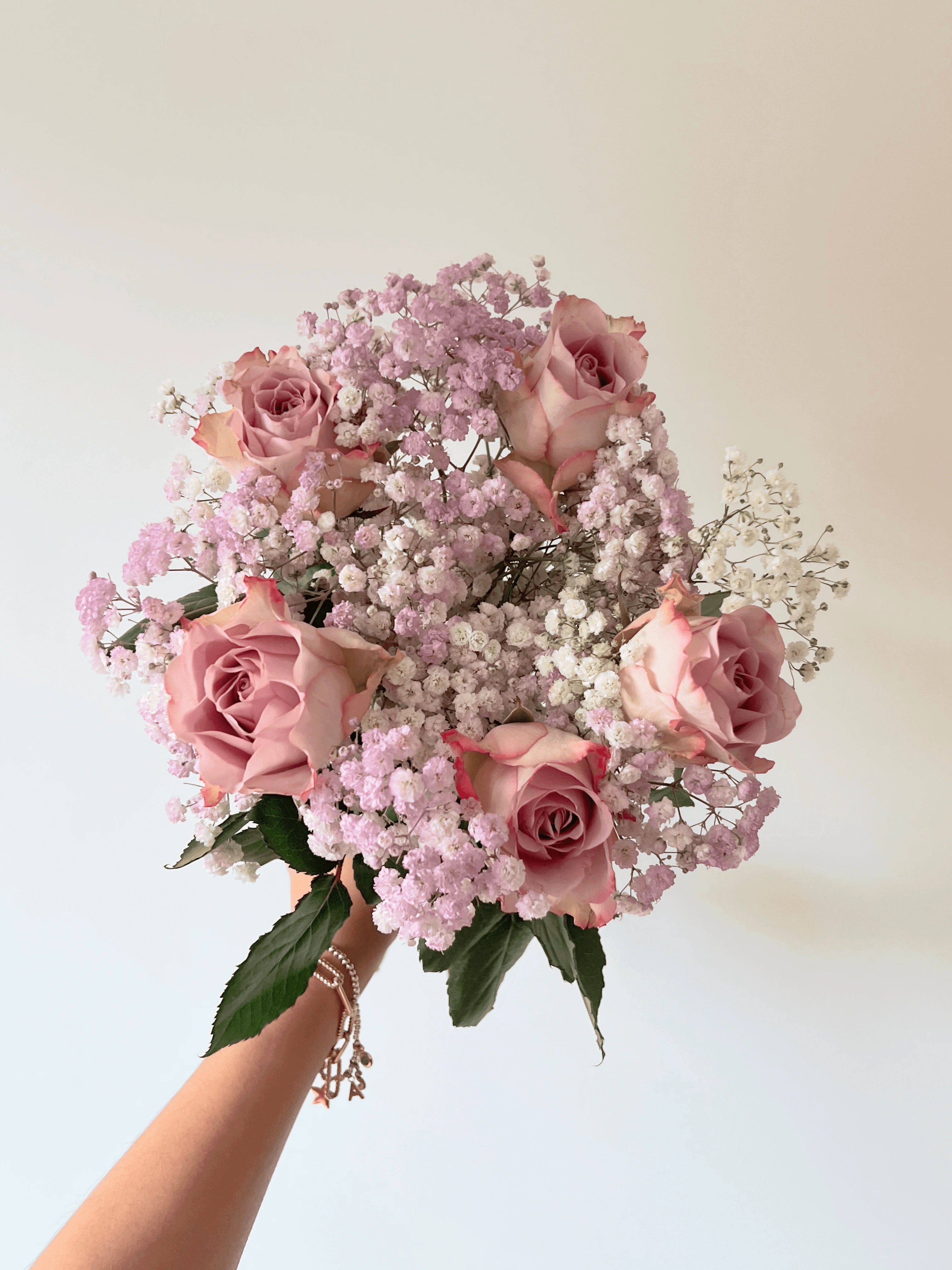 Bouquet of lilac roses and baby's breath held by a hand against a light background. Fairy Bunch | FLOWERFIX
