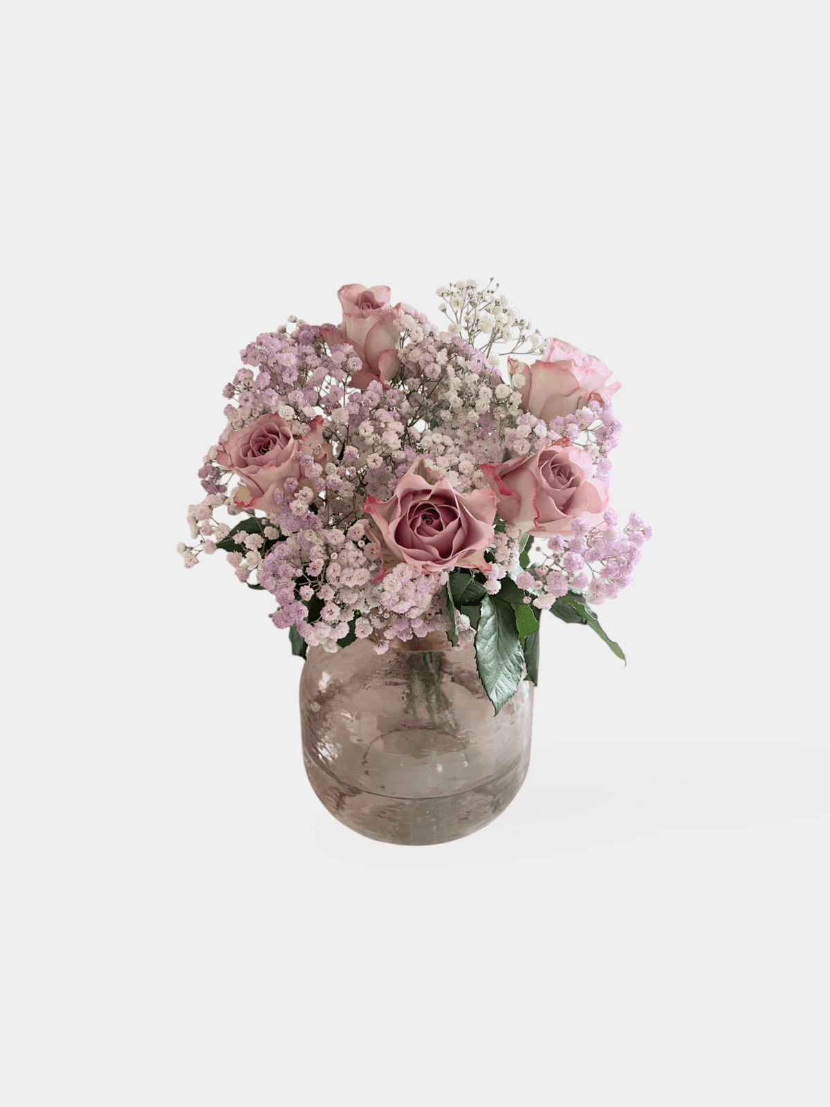 A bouquet of purple and pink flowers, including lilac roses and Baby's Breath, arranged in a clear vase. The Fairy Bunch | FLOWERFIX