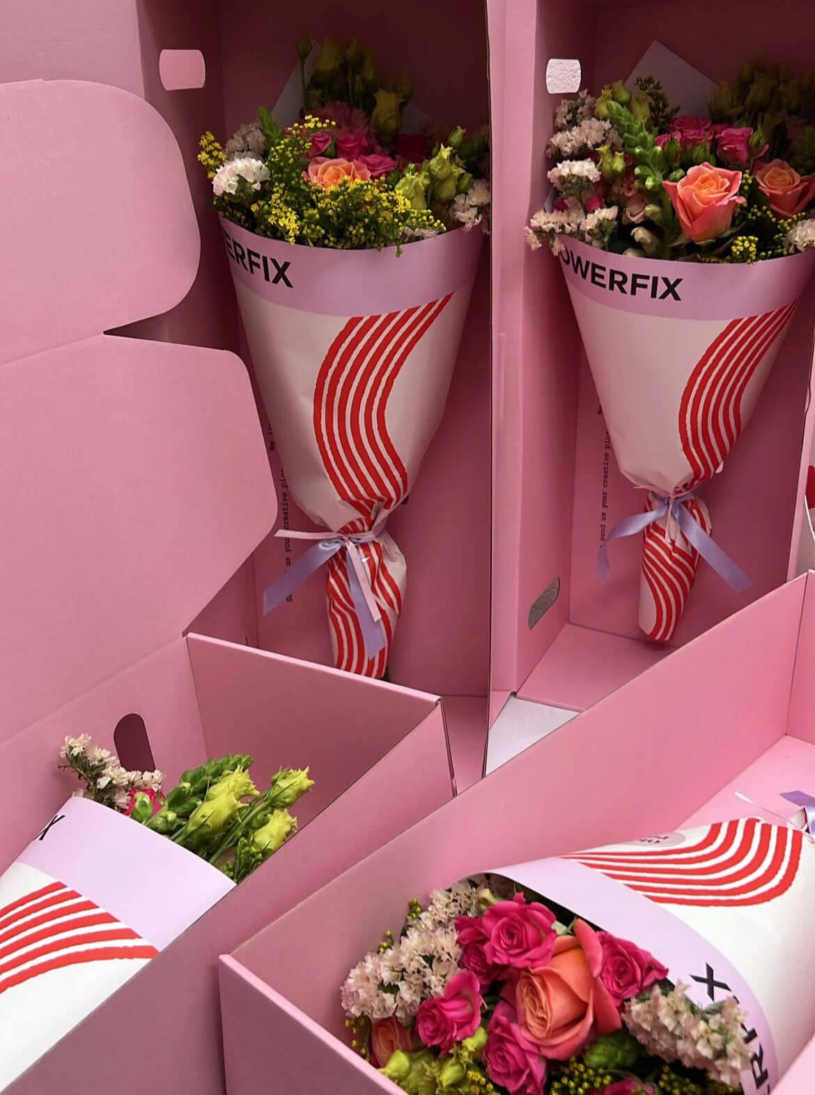 Multiple vibrant, pet-friendly flower bouquets from Flowerfix, featuring safe pink and orange roses, yellow filler flowers, and greenery. The bouquets are securely packaged in stylish pink gift boxes with modern red and white striped wrapping, perfect for pet-loving households.
